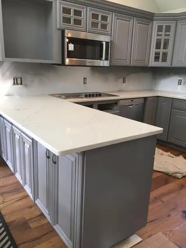 Kitchen with cabinets refinished in a soft gray, white stone counters and stainless appliances