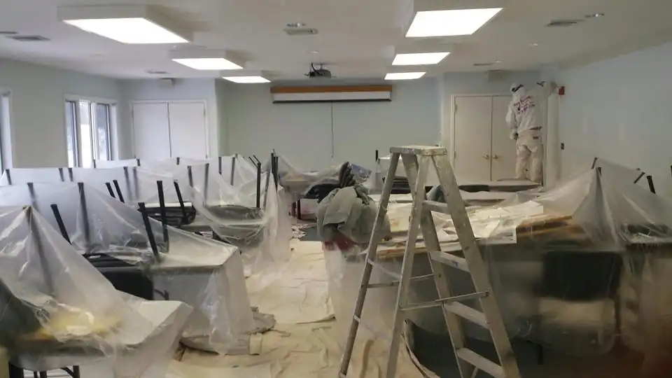 Commercial room covered in plastic while painters mask the walls