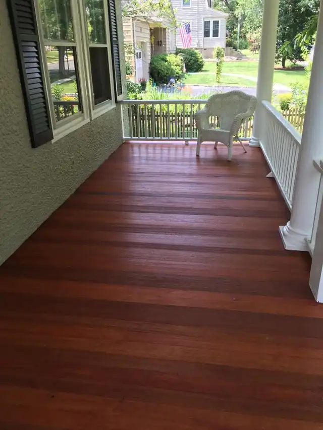 Freshly stained mahogany porch floor running toward white porch posts and railings