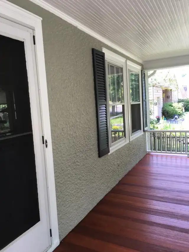 Porch wall with black shutters above a stained porch floor