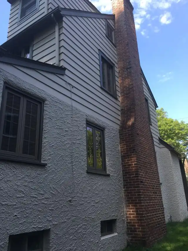 Gray clapboard siding beside a brick chimney with dark trim