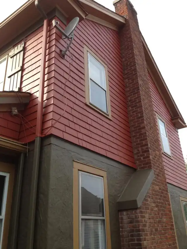 House corner with freshly painted red siding beside gray stucco