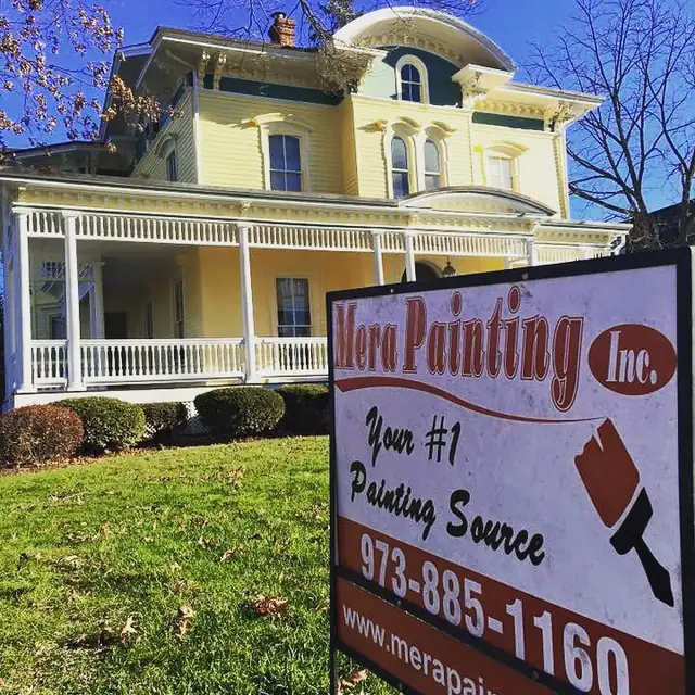 Red Mera Painting Inc. yard sign reading Your #1 Painting Source on the lawn of a yellow Victorian with a wraparound porch