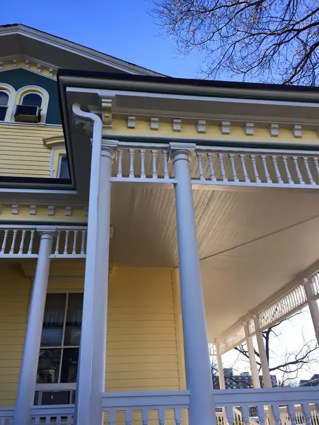Yellow Victorian porch with white columns, teal panels and white bracket trim