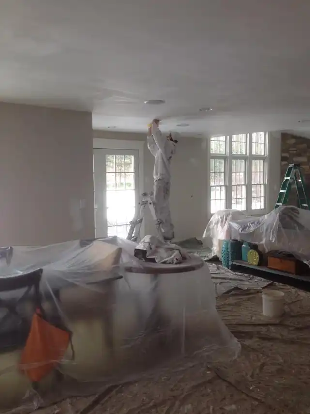 Room fully draped in plastic sheeting with a covered light fixture, prepared before painting