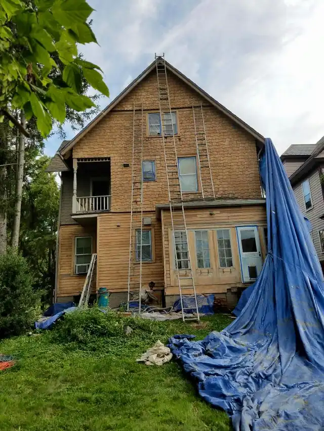 Side of a shingle house with a blue tarp laid down for exterior prep