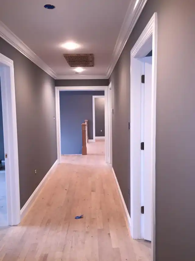 Long gray hallway with white trim and a wood floor