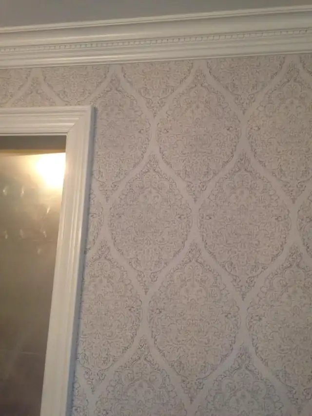 Damask wallpaper hung in a room with white trim around a doorway
