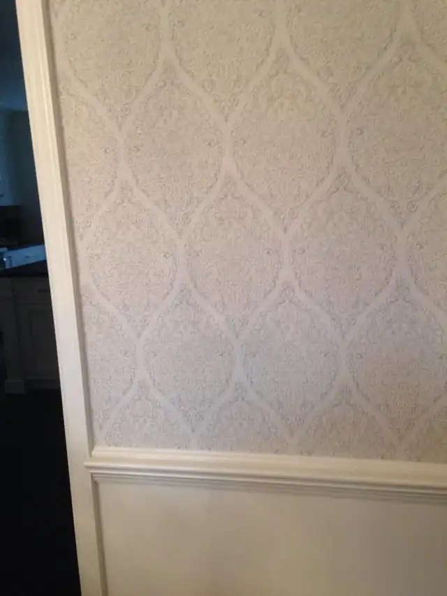 Pale damask wallpaper hung above a white chair rail beside a painted door casing